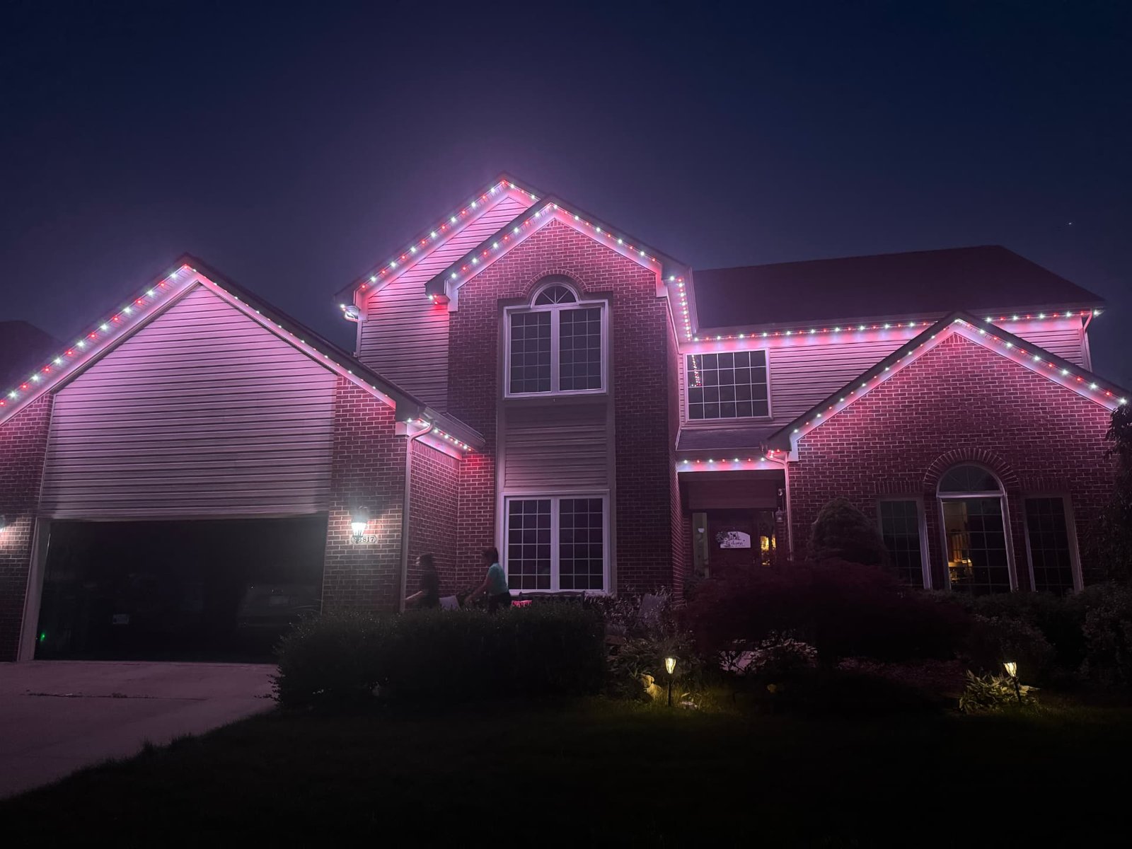 Brick two-story home with pink and white permanent LED roofline lighting